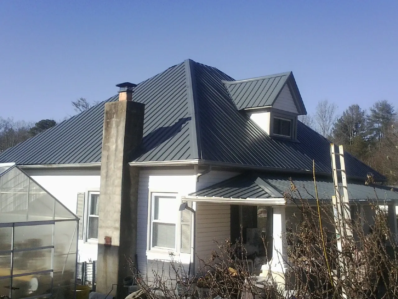 Dark blue standing seam metal roof on a white farmhouse with dormer — Slate & Tile Roof Repair by Roofing Brothers in Grosse Pointe
