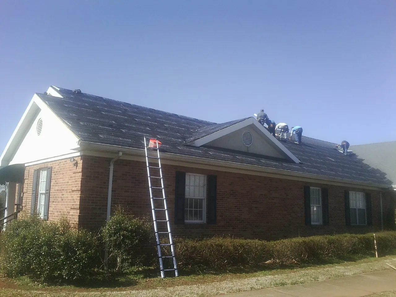 Crew tearing shingles off a brick ranch roof with a ladder set — Emergency Roof Repair work by our crew in Grosse Pointe