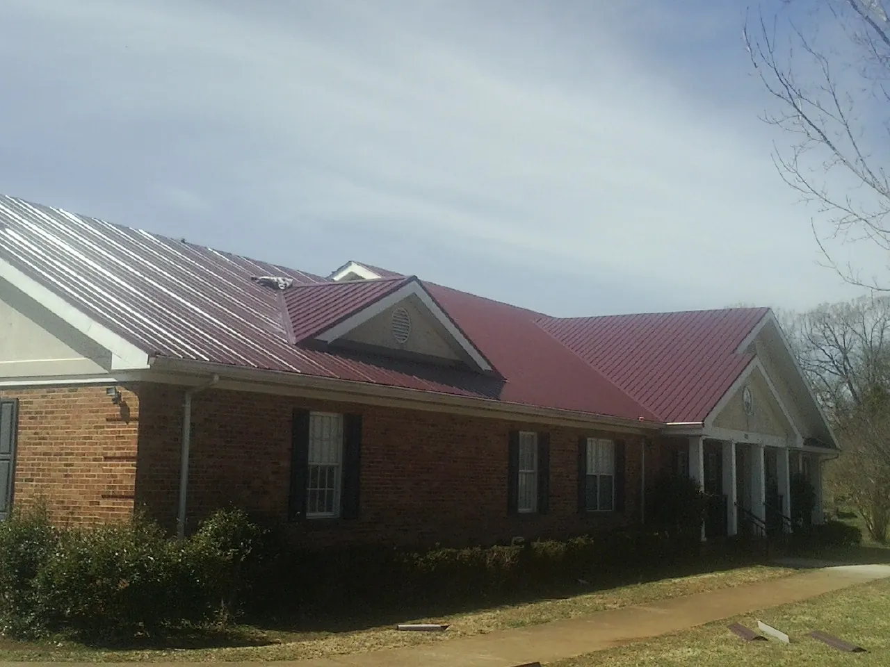 Red metal roof with gabled entries on a long brick building, from a Hail Damage Roof Repair job in Grosse Pointe