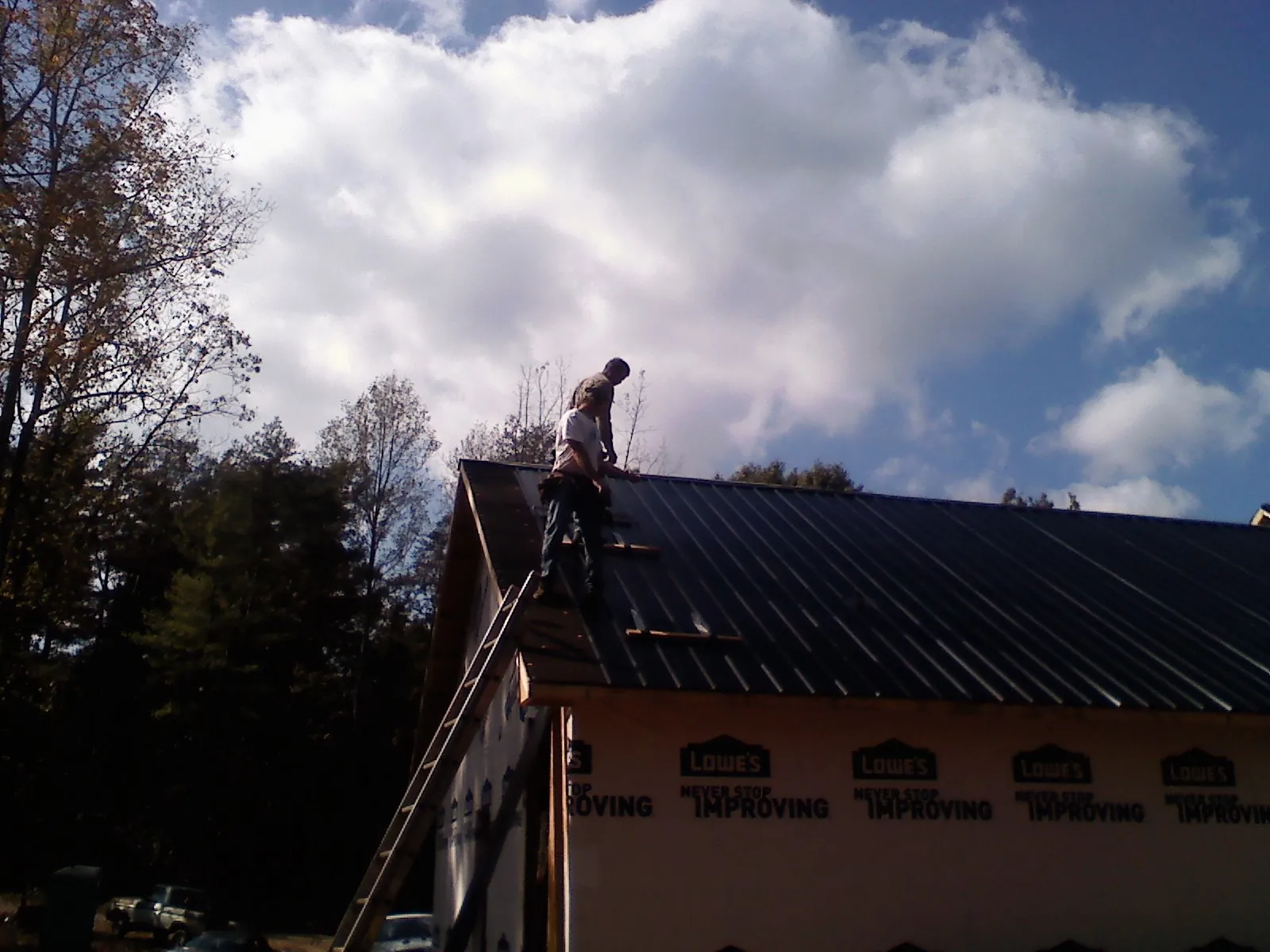 Roofer fastening dark metal panels high against a cloudy sky, from a Roof Inspection job in Grosse Pointe